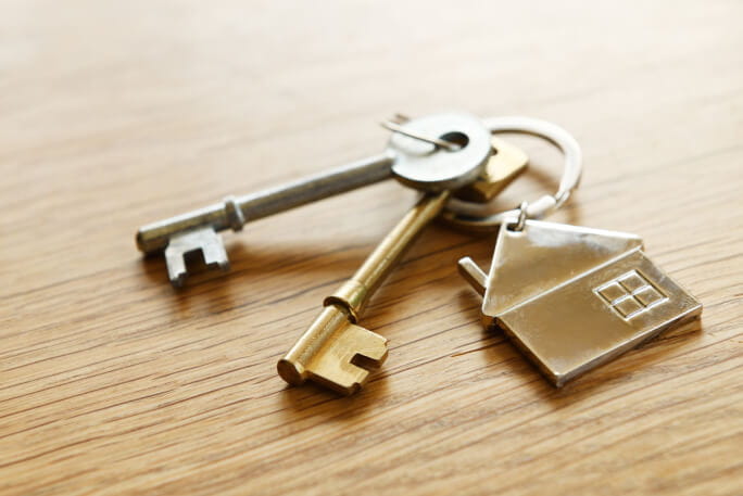 Porta-chaves em forma de casa com duas chaves sobre mesa de madeira 