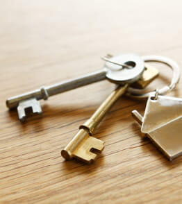 Porta-chaves em forma de casa com duas chaves sobre mesa de madeira