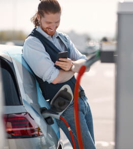 Homem sorridente, encostado ao carro, num posto de carregamento de carros elétricos.
