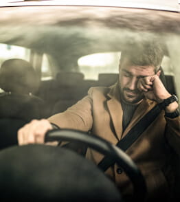 Homem dentro de um carro, em risco de adormecer ao volante.