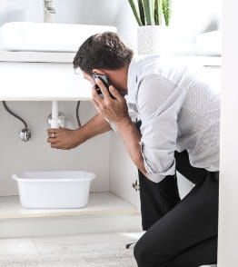 Homem a fazer uma chamada em frente à canalização da casa de banho com fuga de água