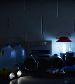 Diversos objetos e produtos úteis em caso de corte de energia, num espaço interior iluminado por velas e lanternas. 