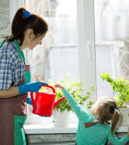 Mãe e filha a regar uma planta em casa 