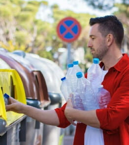 Homem com garrafas de plástico na mão a fazer a separação de lixo no ecoponto