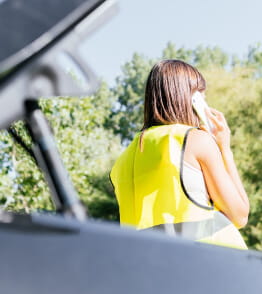 Jovem mulher com colete refletor vestido telefona para fazer a participação de sinistro automóvel após um acidente de carro. 