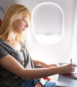 Jovem mulher sentada num avião a escrever 