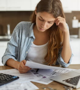 uma jovem em frente a um computador faz contas para decidir se deve fazer um empréstimo para pagar as dívidas 