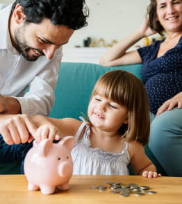 O pai e a mãe grávida ensinam a filha pequena a poupar dinheiro com um porquinho mealheiro 