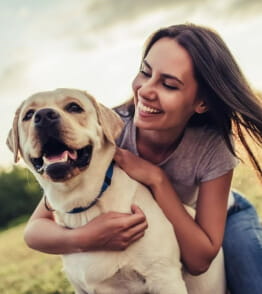 Mulher sorridente agarrada a um cão no meio do campo