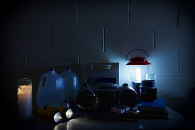 Diversos objetos e produtos úteis em caso de corte de energia, num espaço interior iluminado por velas e lanternas. 