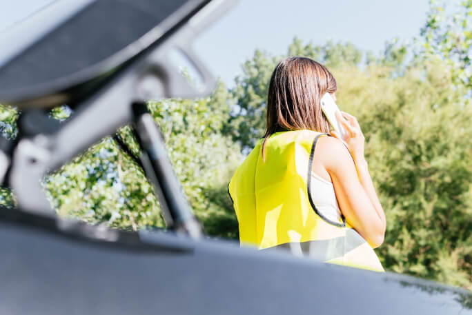 Jovem mulher com colete refletor vestido telefona para fazer a participação de sinistro automóvel após um acidente de carro. 