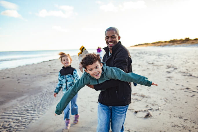 Um pai brinca perto de dois filhos na praia, para sua proteção  