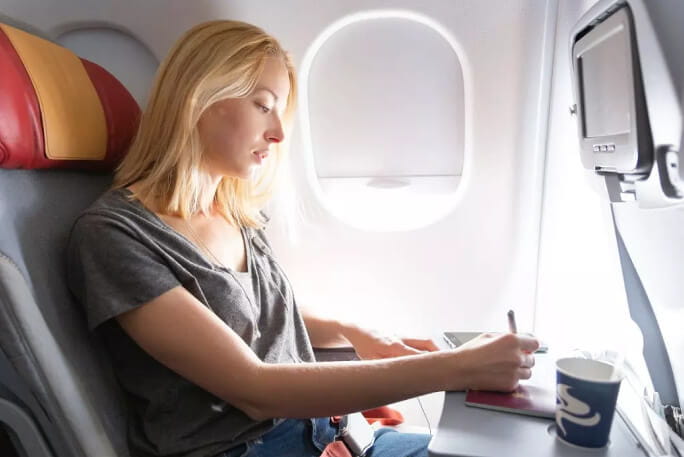 Jovem mulher sentada num avião a escrever 