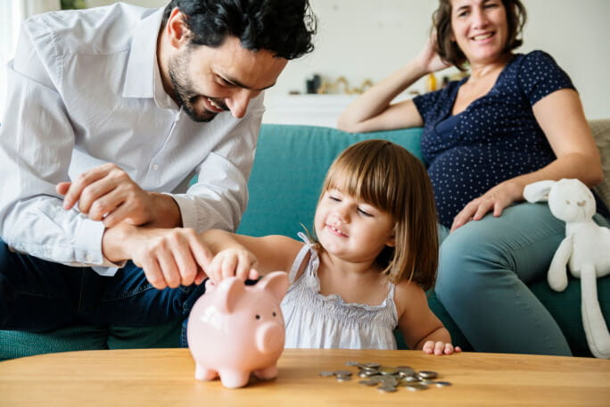 O pai e a mãe grávida ensinam a filha pequena a poupar dinheiro com um porquinho mealheiro 