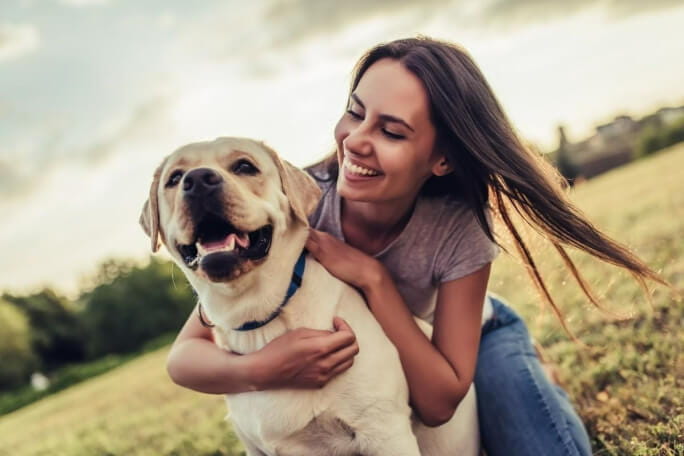 Mulher sorridente agarrada ao cão no meio do campo