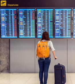 Uma rapariga de costas, num aeroporto, consulta o painel das partidas à procura da sua viagem.