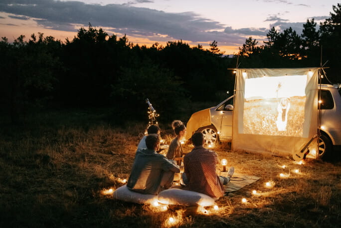 Grupo de amigos em férias de verão assiste a uma sessão de cinema privada ao ar livre. 