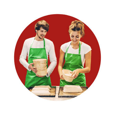 Casal com avental verde a cozinharem pão em tabuleiros.