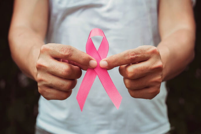 Duas mãos masculinas seguram o laço rosa do cancro da mama. 
