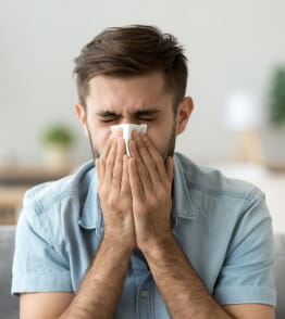 Jovem com alergia ou uma constipação espirra tapando o nariz com um lenço. 