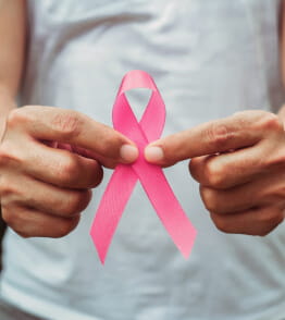 Descrição Duas mãos masculinas seguram o laço rosa do cancro da mama.