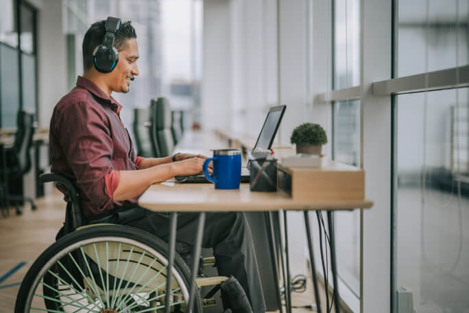 Pessoa com deficiência, sentada numa cadeira de rodas, trabalha online. 