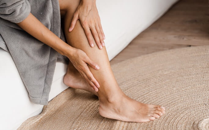 Mãos de mulher a massajar as pernas para aliviar a retenção de líquidos.